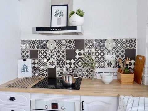 Modern kitchen with geometric patterned black and white backtile, wooden countertop, open shelving with plants and decor above stove